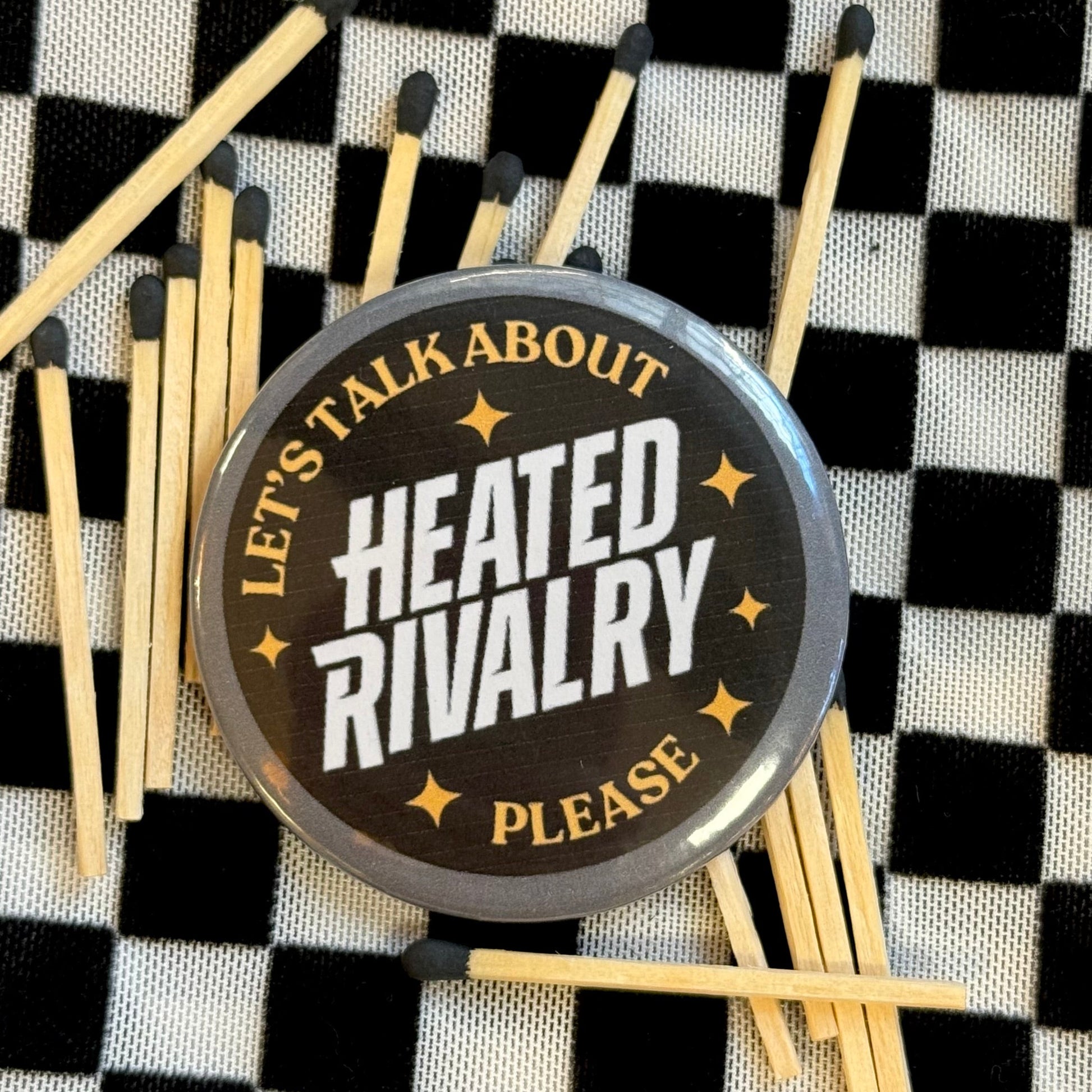 Matches with a round metal token labeled 'Let's talk about heated rivalry please' on a checkered background