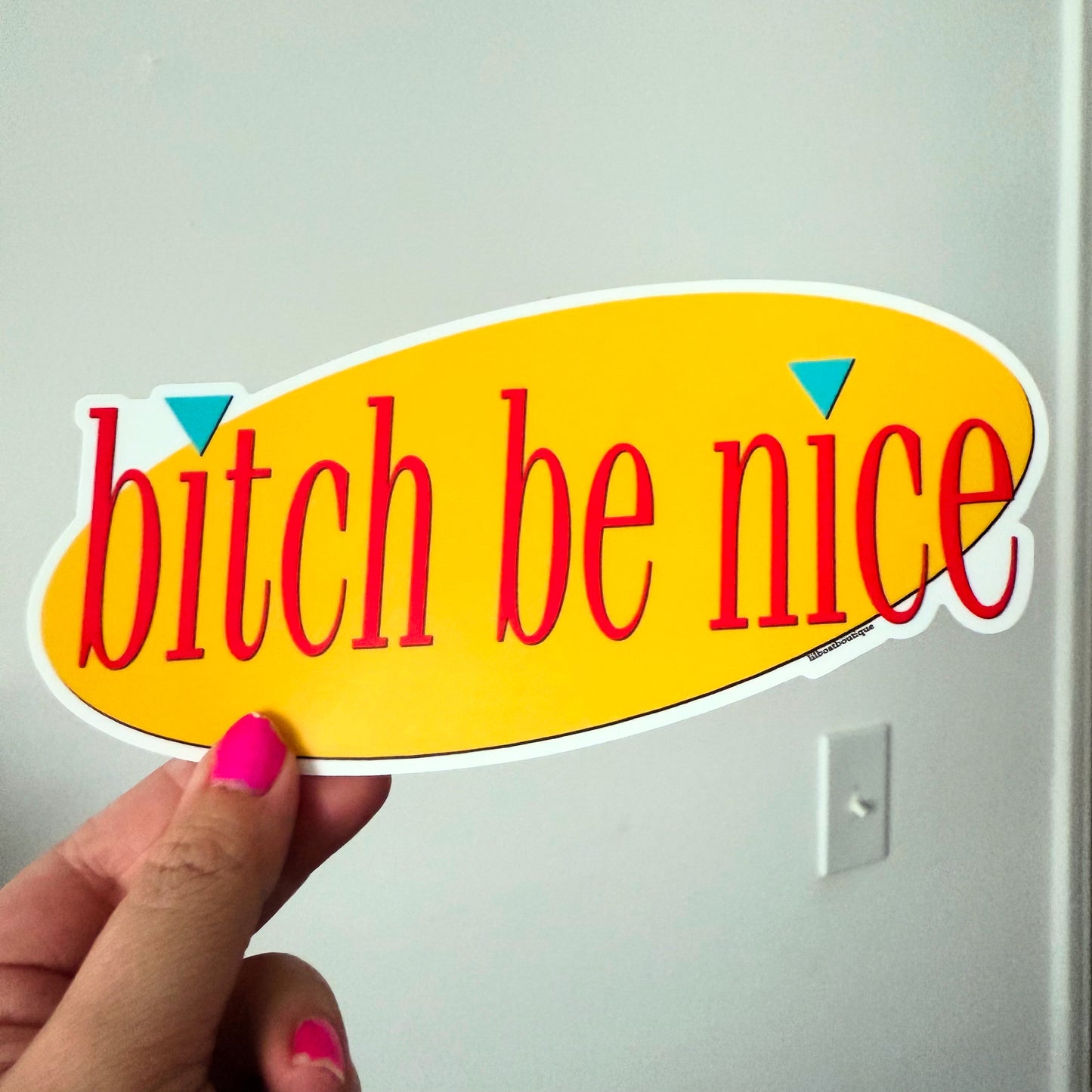 Sticker with 'bitch be nice' text held by a hand against a white background