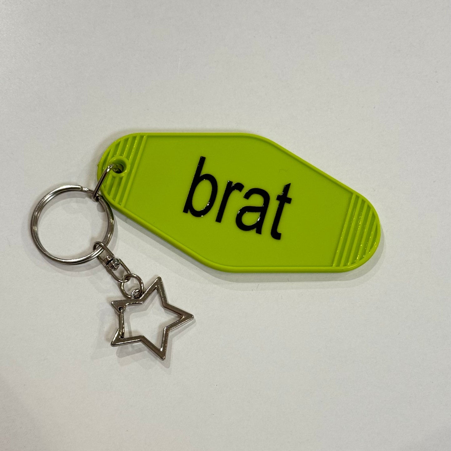 Keychain with a green tag labeled 'brat' and a star charm on a white background