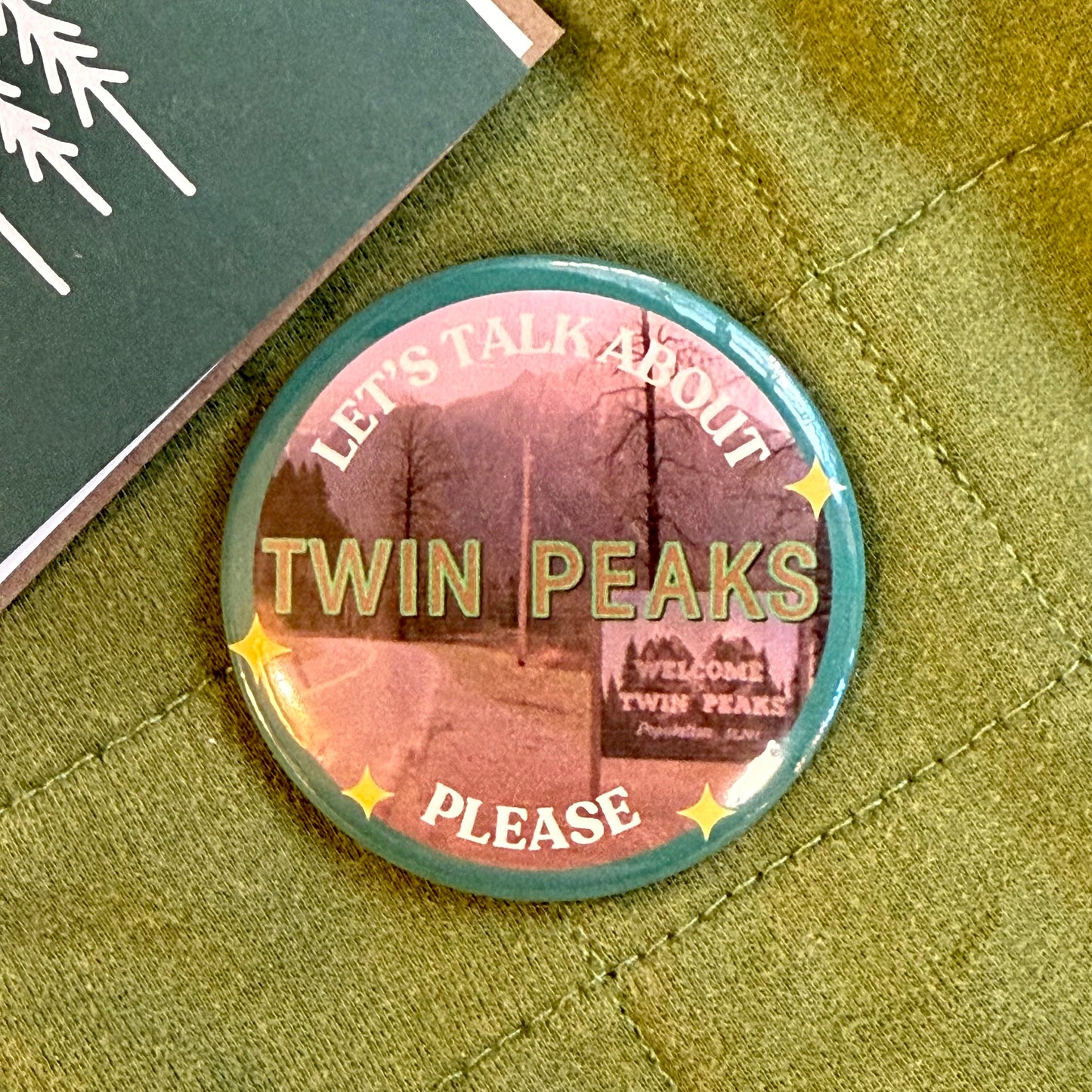 Button badge with Twin Peaks text on a green fabric background